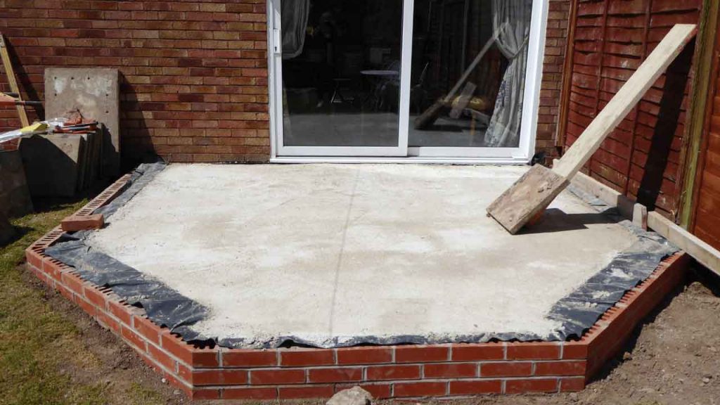 Freshly poured concrete patio slab against a brick home, mid-construction