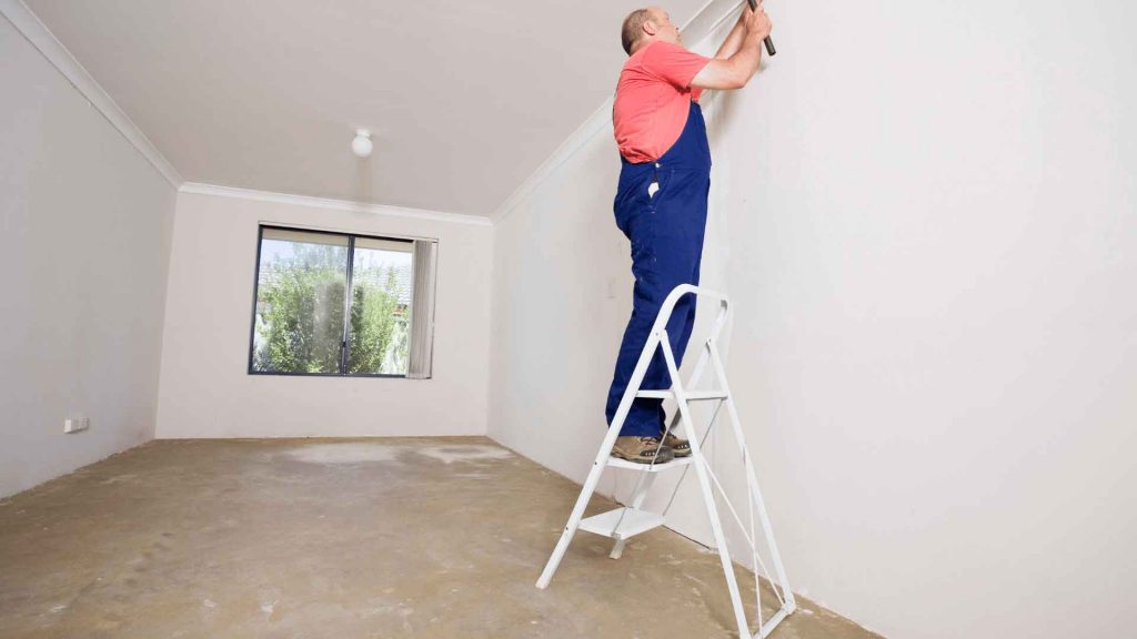 Tradesperson finishing a wall corner on a stepladder in an empty room