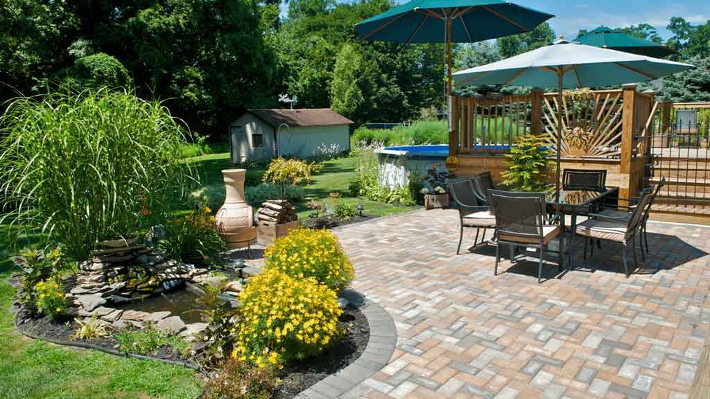 Paved backyard patio with outdoor dining furniture and garden landscaping
