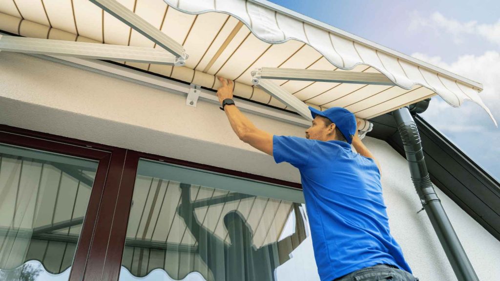Tradesperson installing a retractable fabric awning on a building