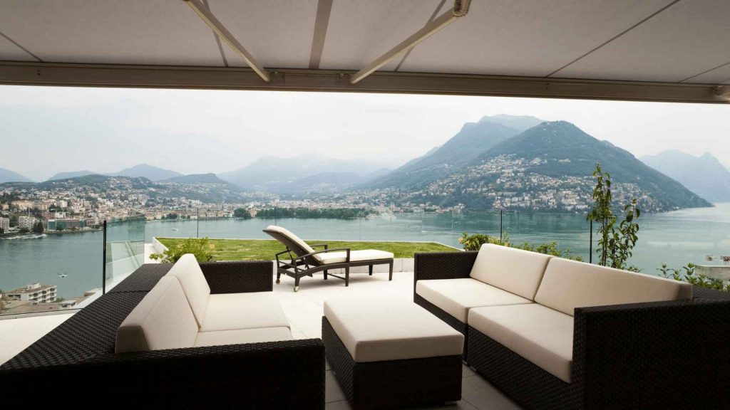 Covered terrace with a retractable awning overlooking a lake and hills