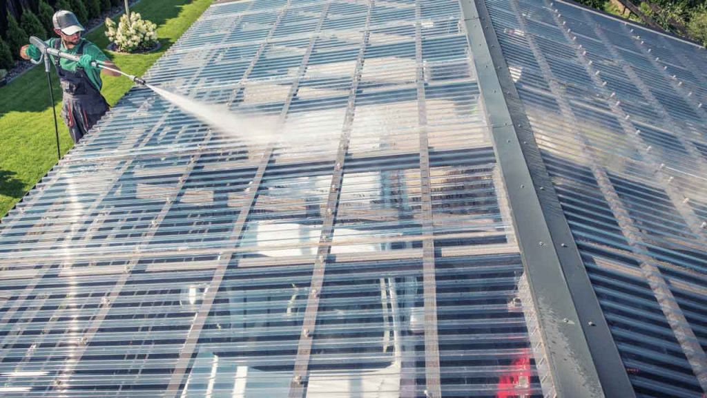 Tradesperson cleaning a polycarbonate patio roof with a pressure washer
