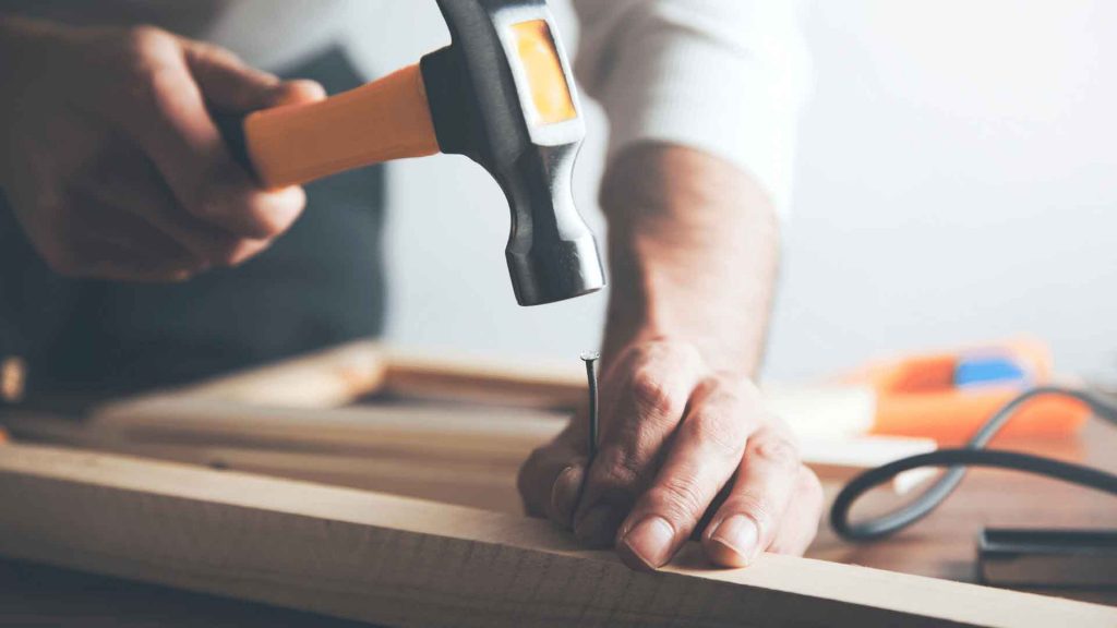 Close-up of hands hammering a nail into a timber frame