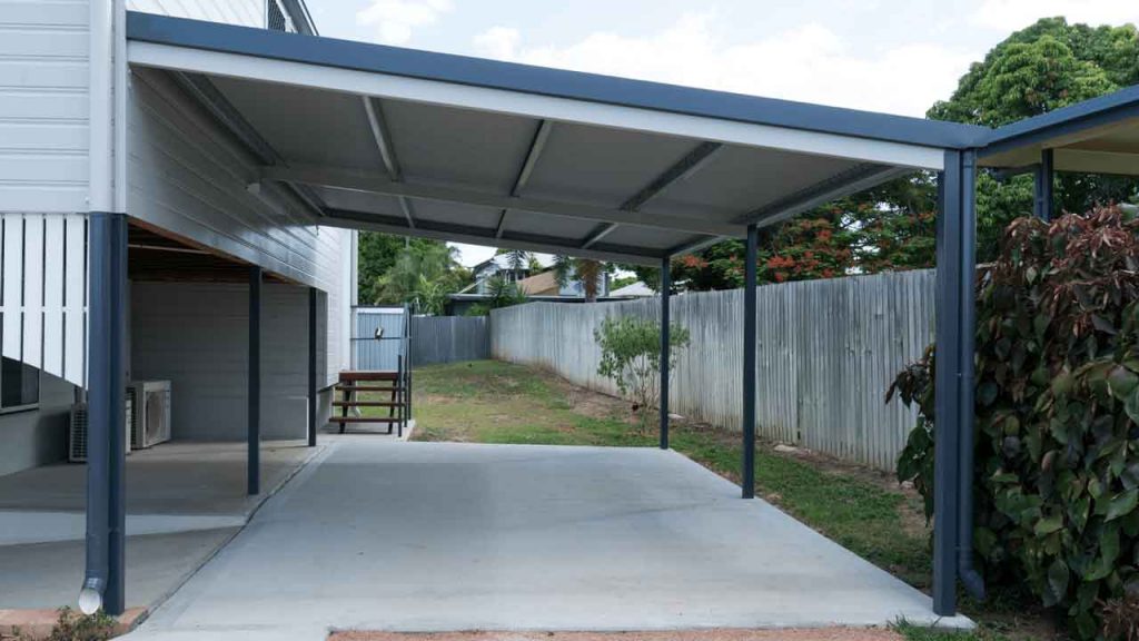 Completed steel-framed carport attached to a home, sheltering a driveway