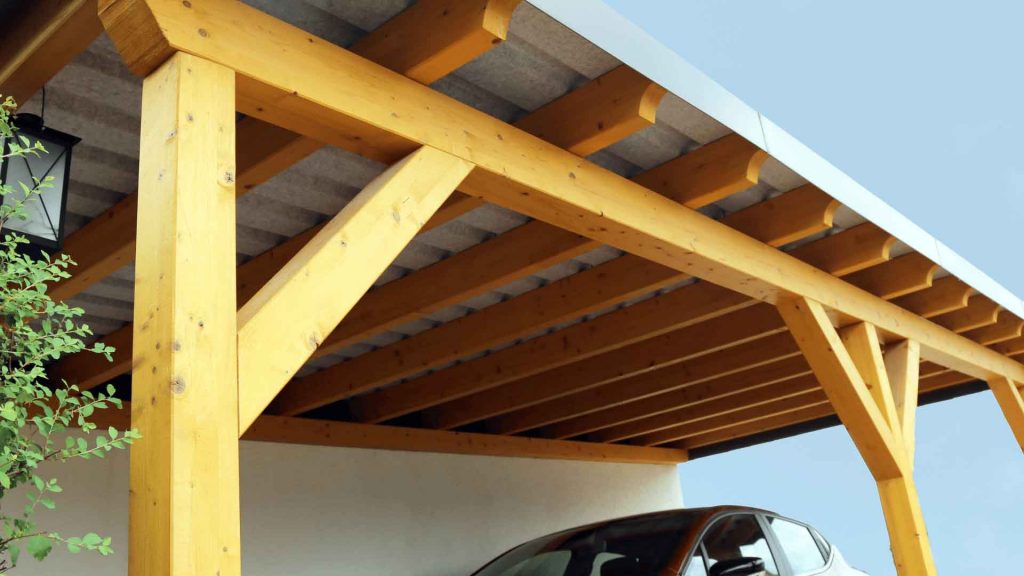 Timber-framed carport roof structure sheltering a parked car