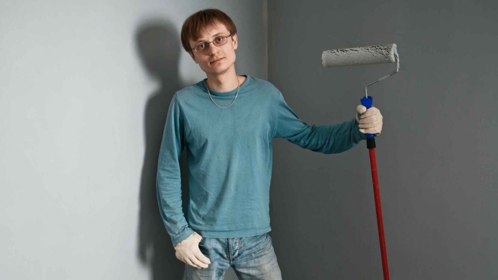 Tradesperson holding a paint roller against a wall