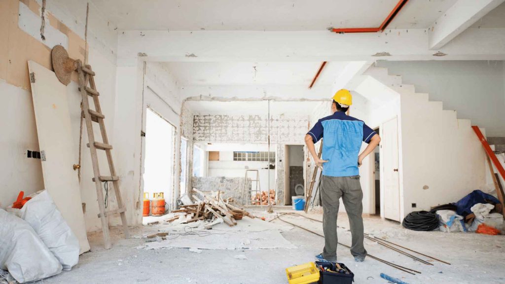 Tradesperson in hard hat surveying a stripped-back room mid-renovation