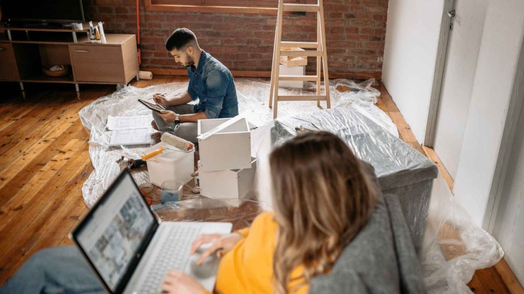 Two people reviewing renovation plans on a laptop in a room being renovated