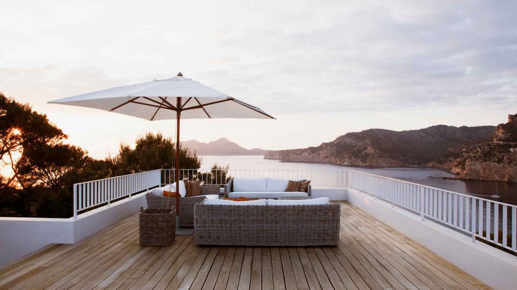 Outdoor deck with lounge seating overlooking water and hills at sunset